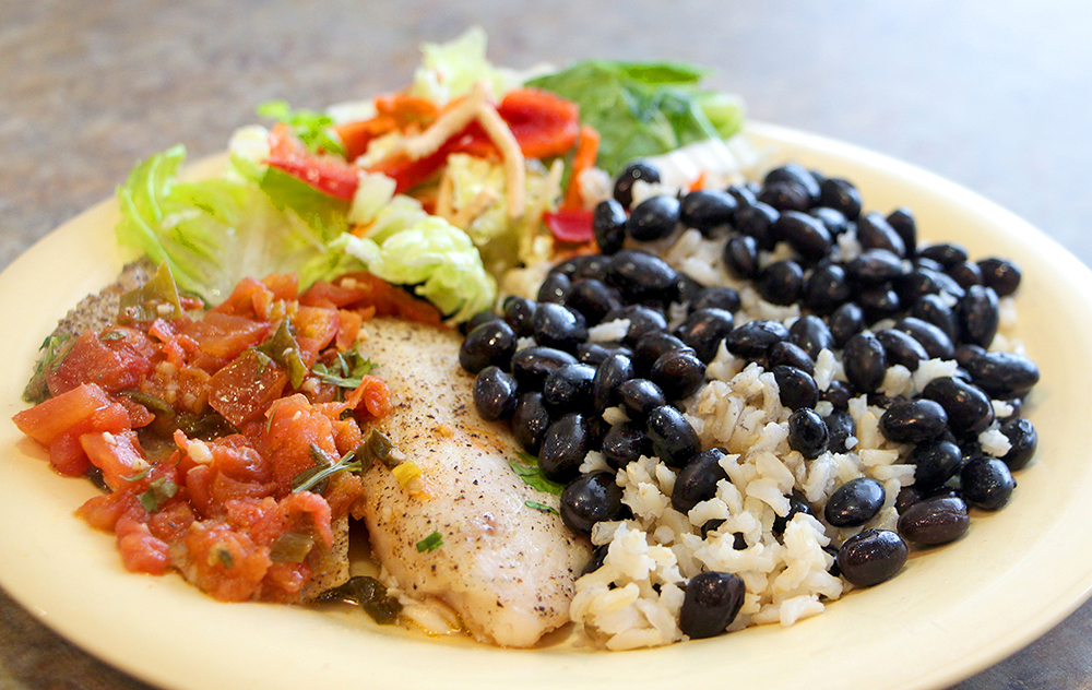 A plate of tilapia with tomatoes, beans, and salad.