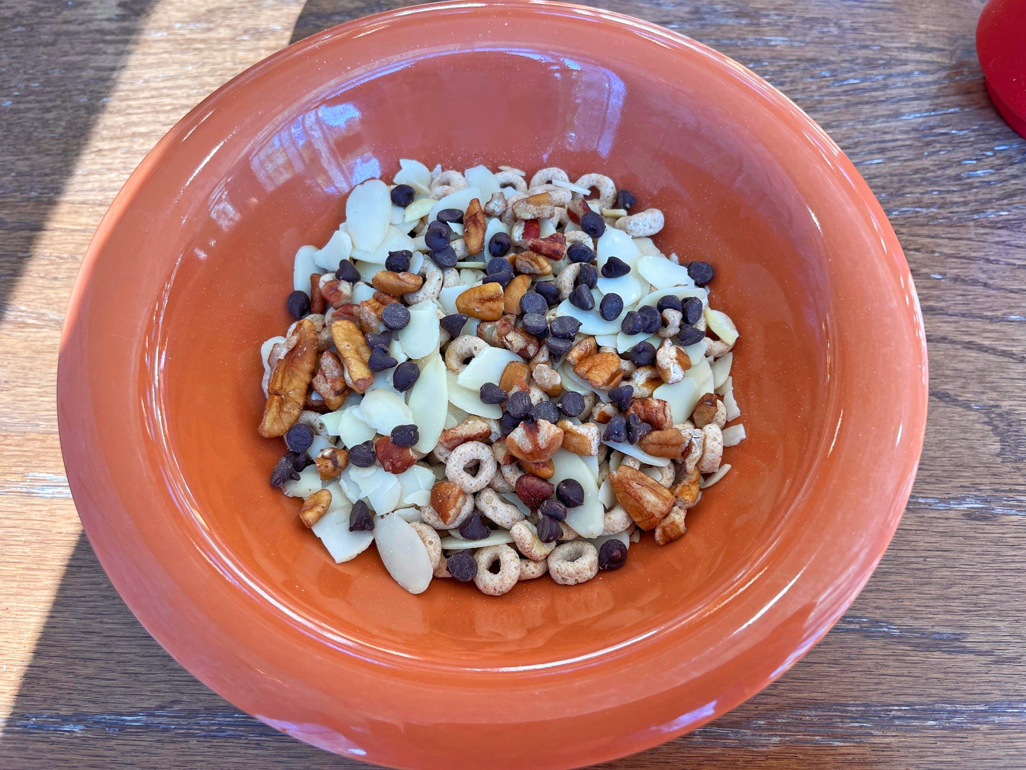 A photograph of a bowl filled with chopped almonds and walnuts, chocolate chips, and cherios.