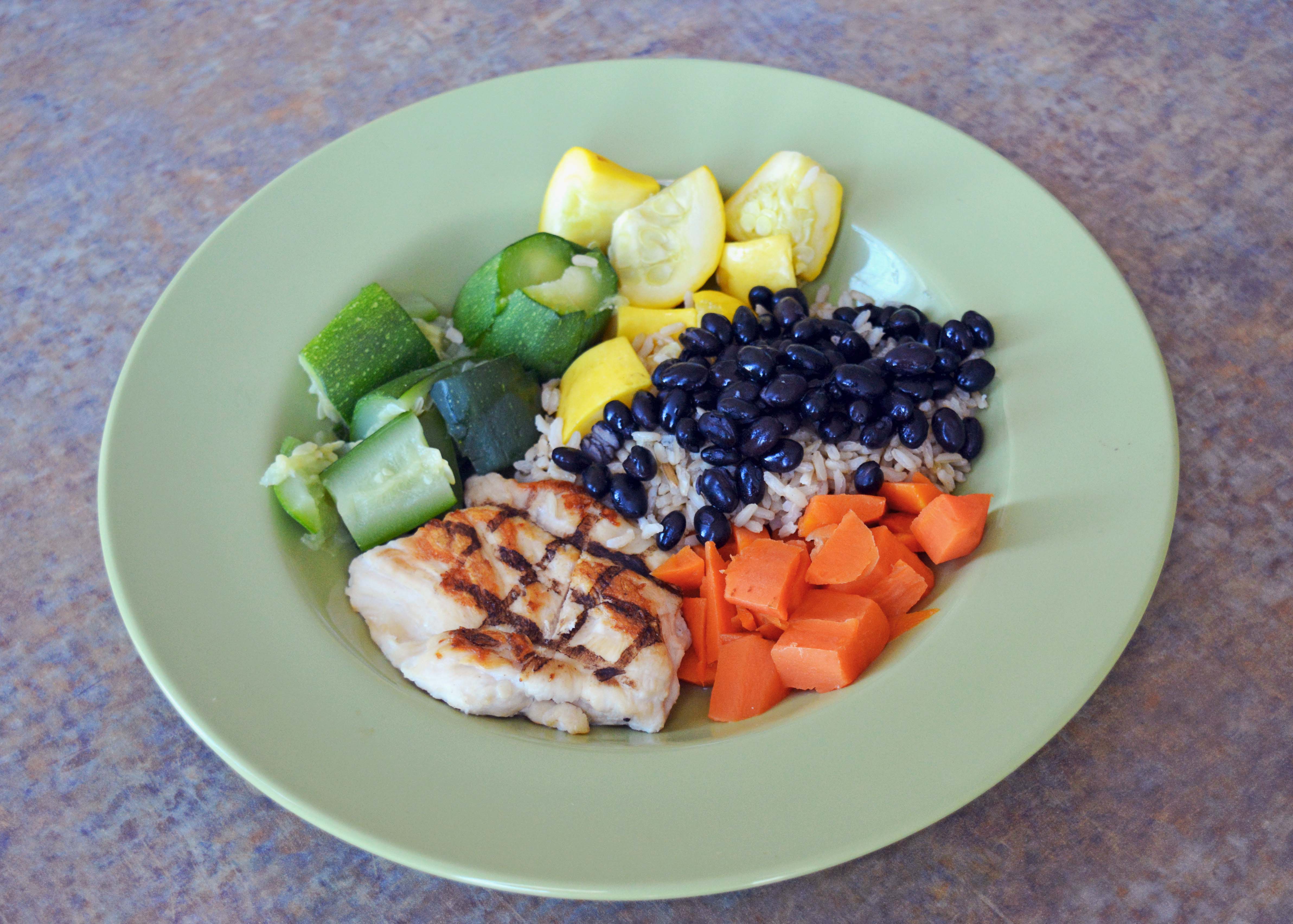 a green shallow bowl with grilled chicken, rice, black beans, and diced sweet potatoes, squash, and zucchini