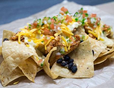 A photograph of nachos with cheese, chicken, beans, and pico topping.