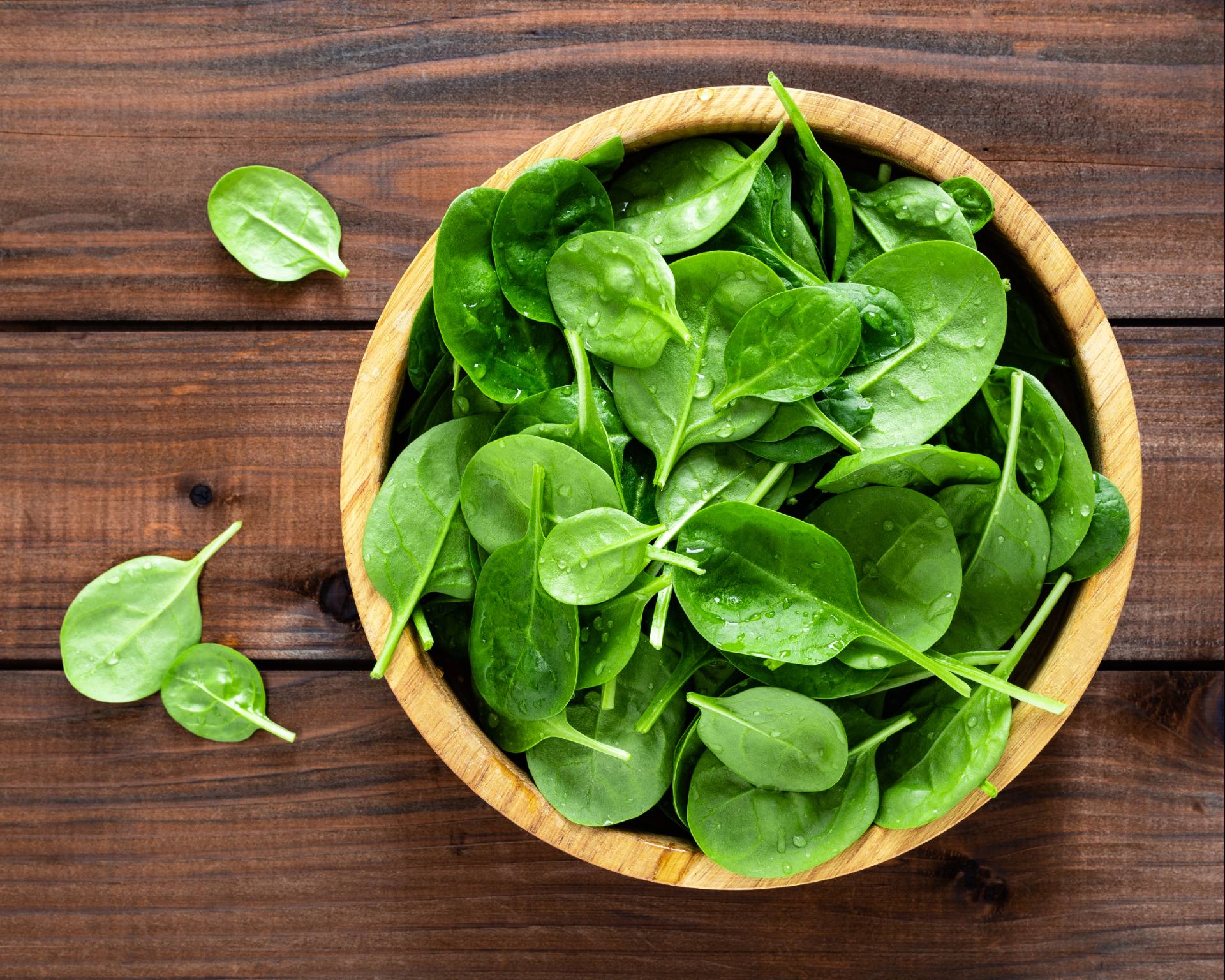 A photograph of a bowl of fresh spinach on a wooden background.