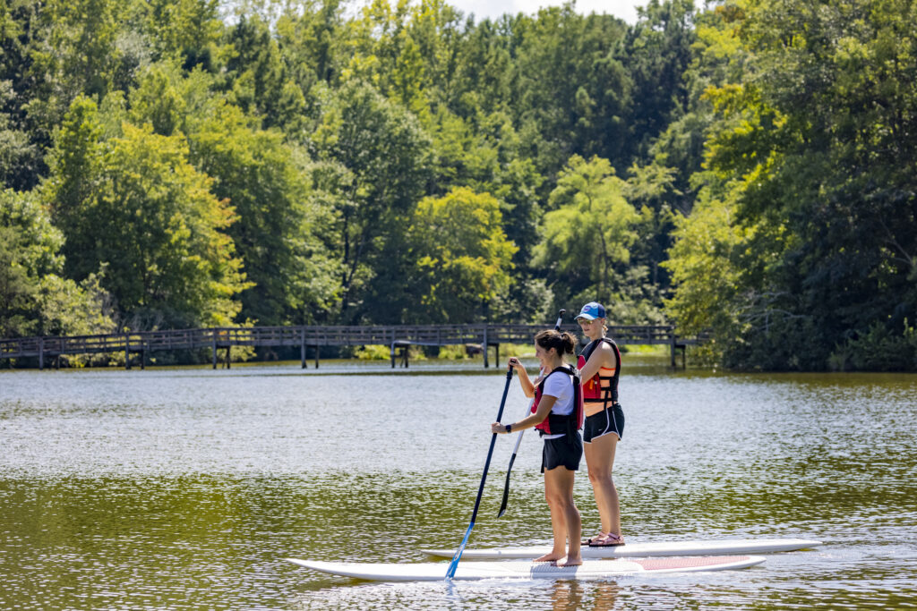 (L-R) Undergraduate students Sierra Shippee and Mercedes Bangs enjoy an afternoon on Lake Herrick on paddleboards.