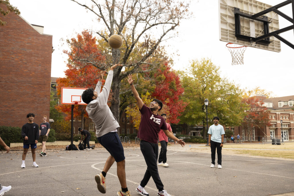 Students play a game of pickup basketball on the courts at Myers Hall with fall foliage on the trees in the background.