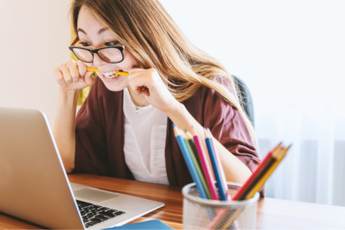 Image of a woman chewing a pencil while looking at her laptop.