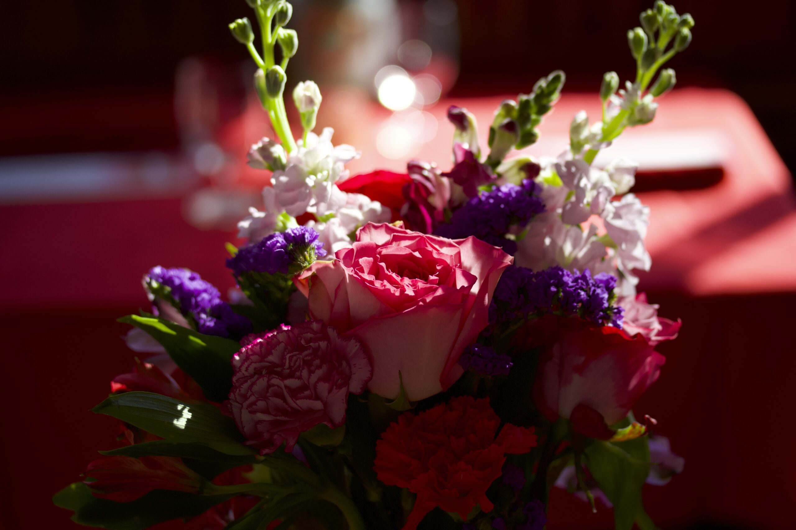 Photo of a bouquet of flowers in the foreground and a table covered in a red tablecloth in the background.