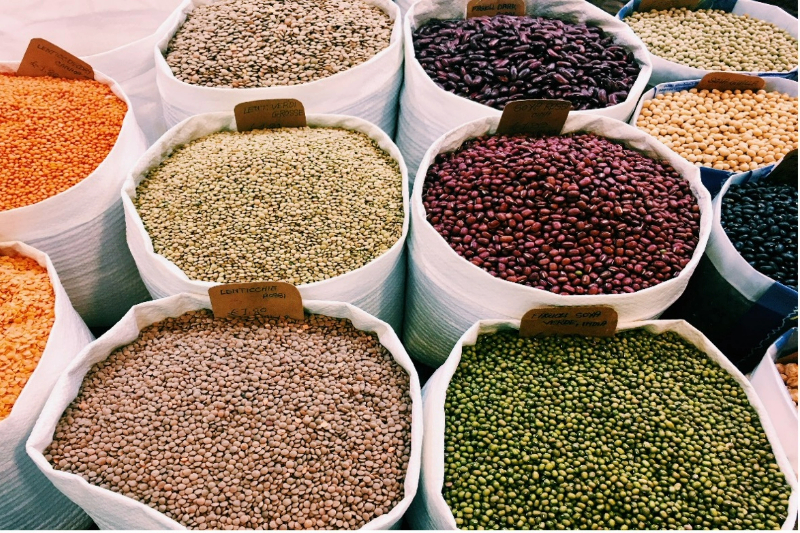 A photograph of a variety of beans sorted into large, open bags