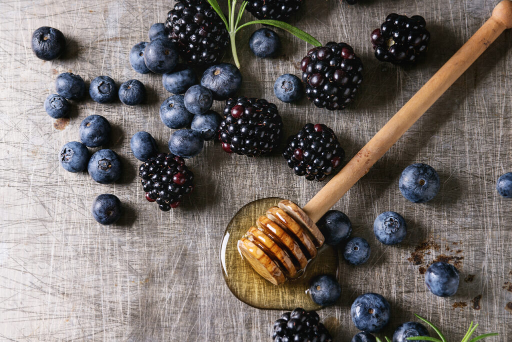 Berries blackberry and blueberry, honey on dipper, rosemary served over gray metal texture background.