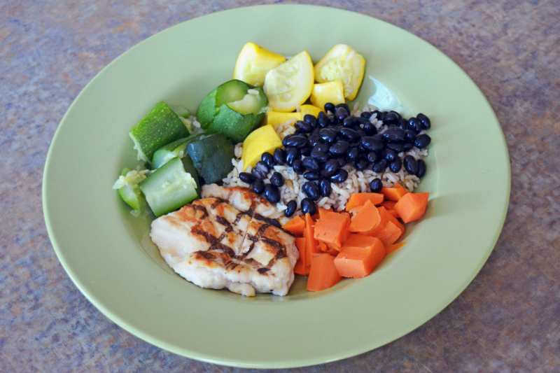 a green shallow bowl with grilled chicken, rice, black beans, and diced sweet potatoes, squash, and zucchini