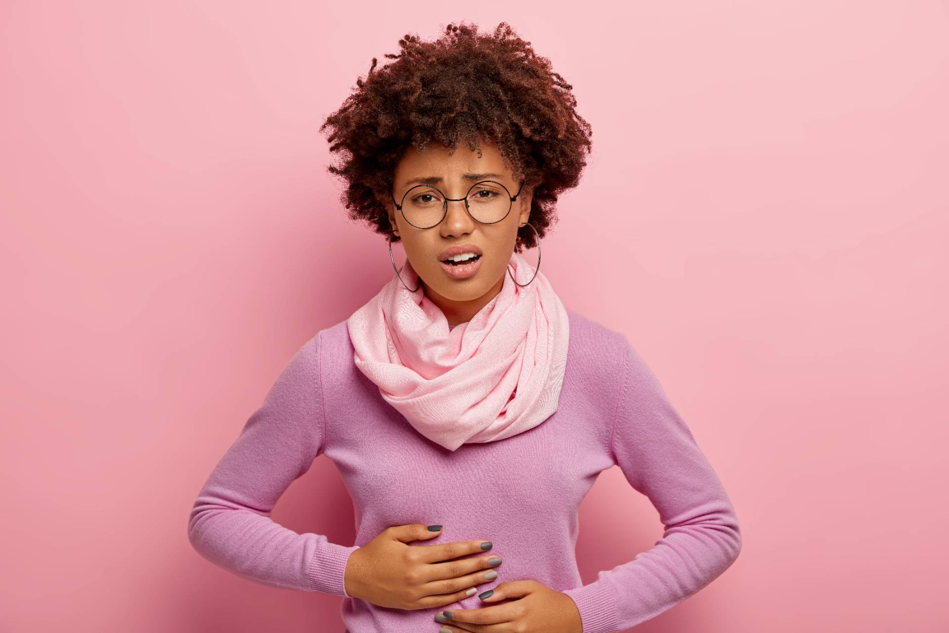 A photograph of a woman making an upset face at the camera and holding her stomach.