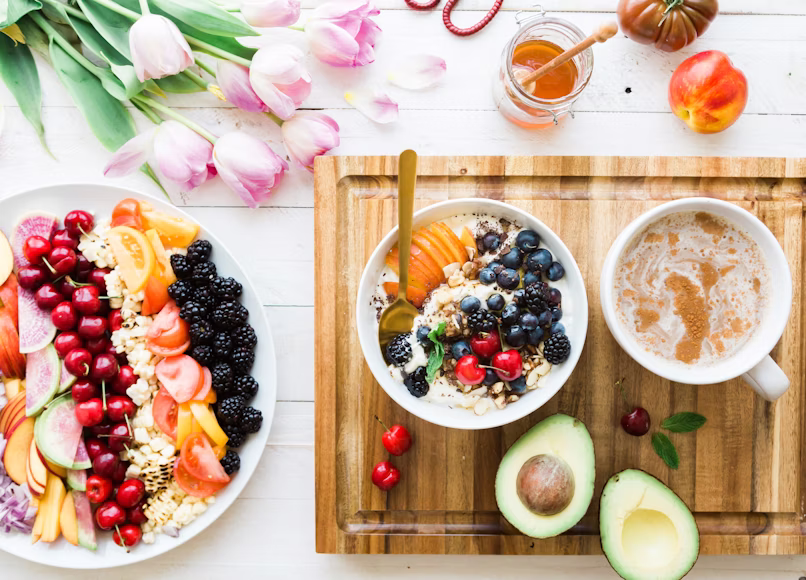 bowl of yogurt and fruit on a cutting board with a cut avocado and cherries.