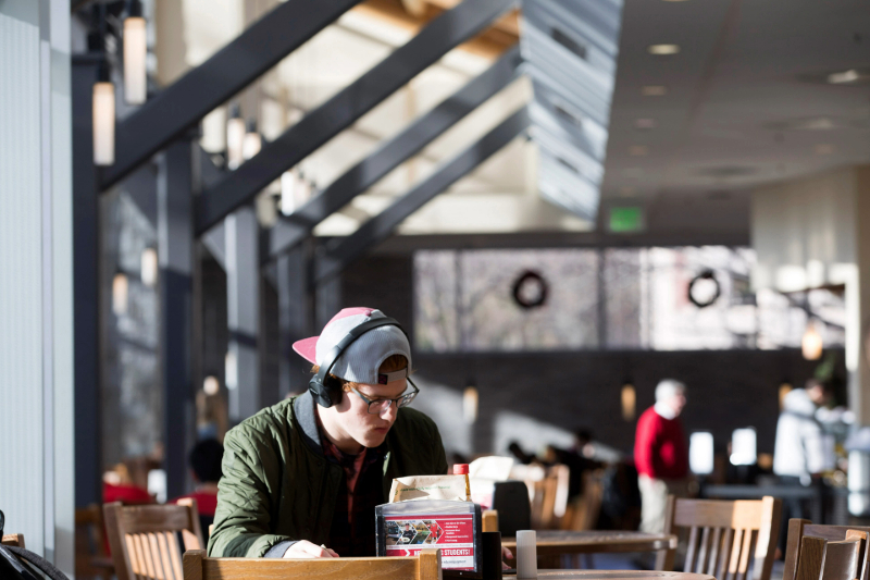 a student wearing a hat and headphones sits studying at a table in Bolton Dining Commons.